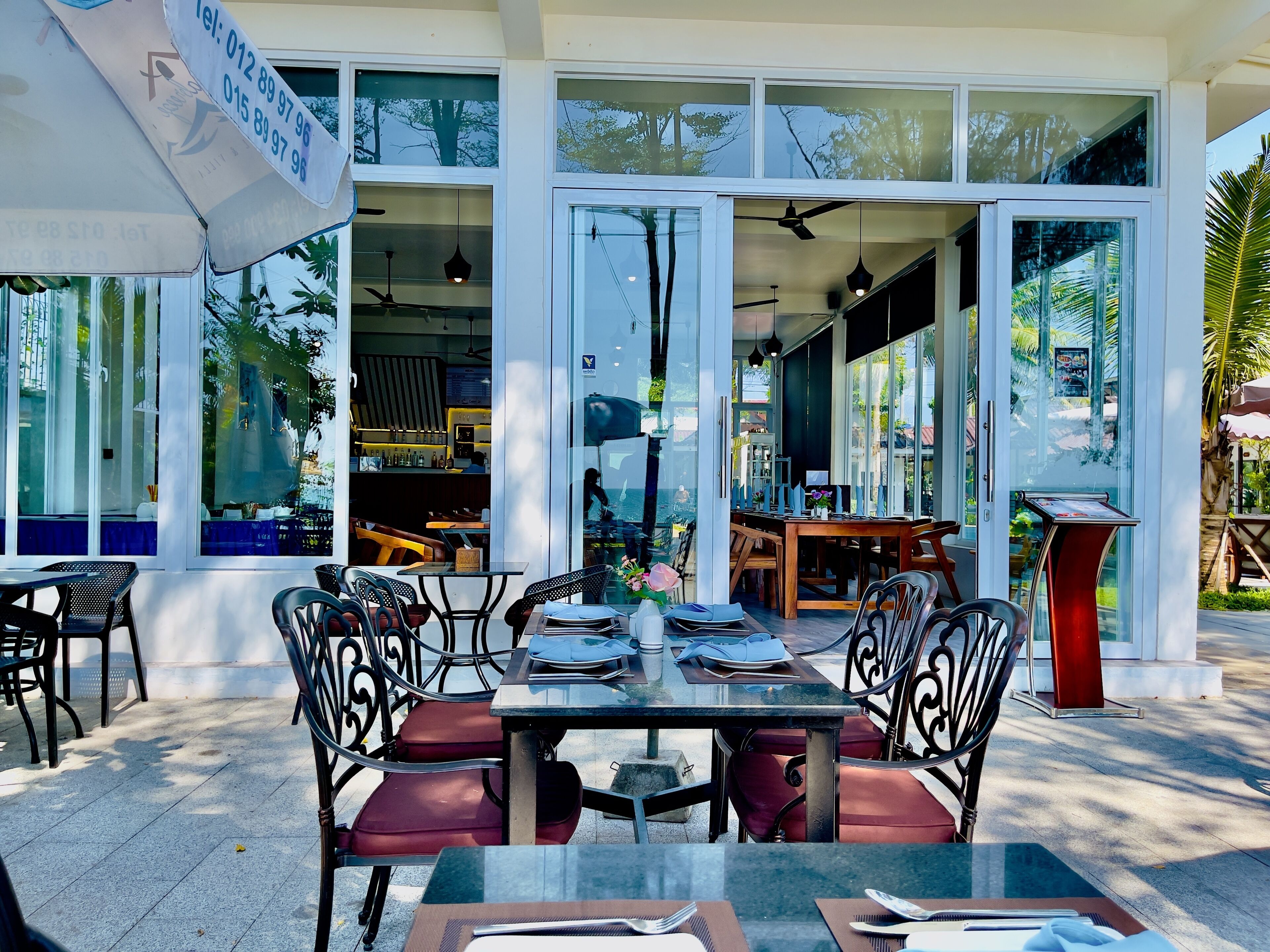 An outdoor seating area with tables and chairs, large windows, and a view of the interior.