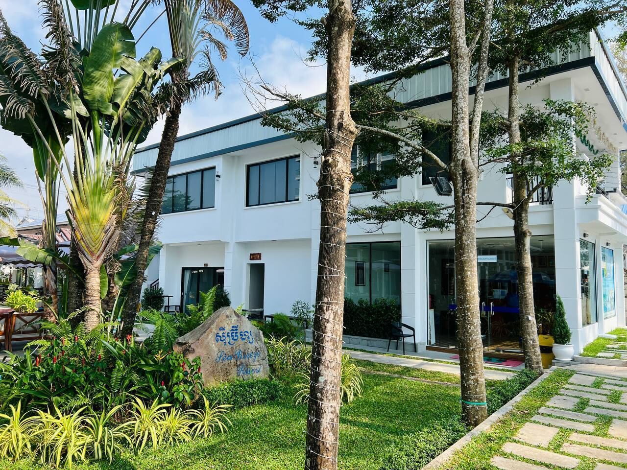 Un bâtiment moderne à l’extérieur blanc, entouré d’une végétation luxuriante et de palmiers.