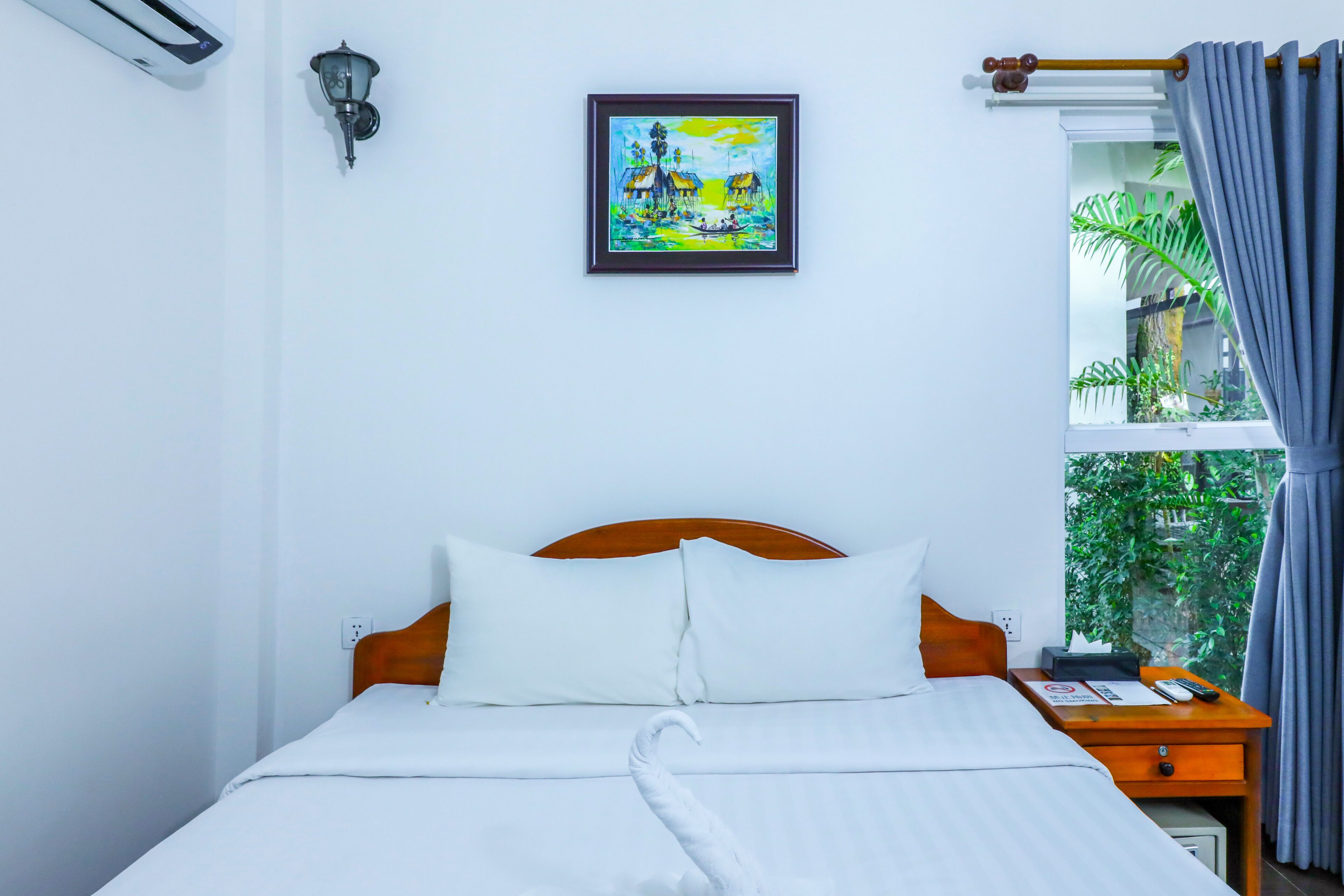 Ein Hotelzimmer mit Bett, Nachttisch, einem gerahmten Gemälde, einem Vorhangfenster und einer Klimaanlage.