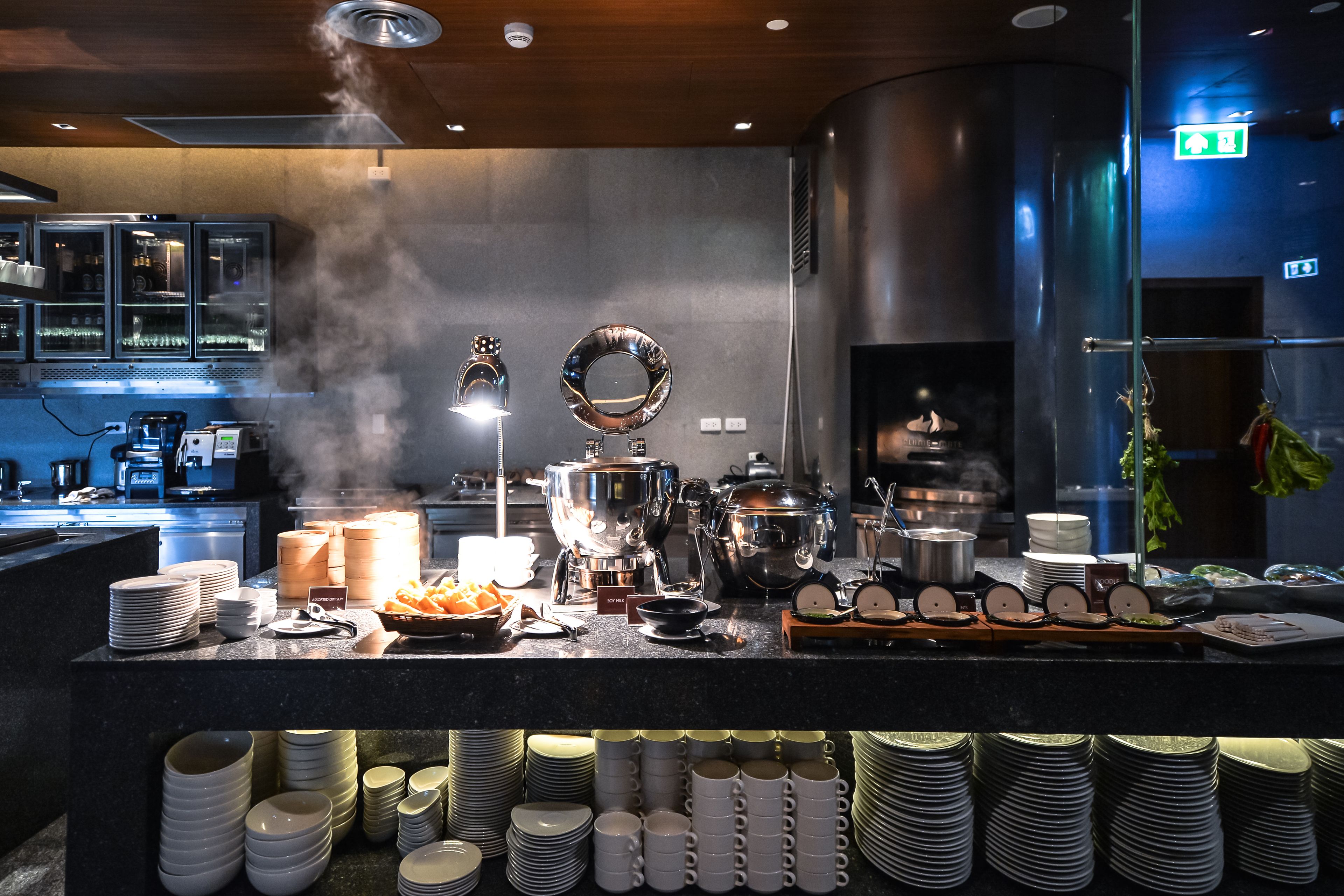 A buffet setup with various dishes, utensils, and stacked plates.
