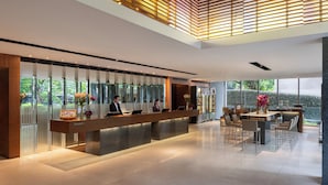 Zona de recepción moderna de hotel, con mostrador, personal y área de descanso con vista a áreas verdes.