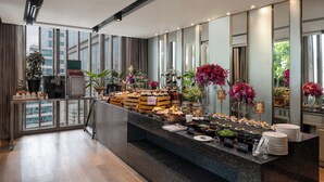 Un moderno vestíbulo de hotel con una zona de buffet central, ventanas amplias y vistas a la ciudad.