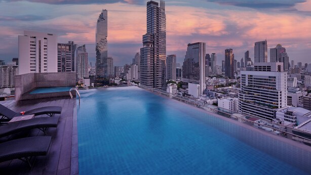 Una piscina en la azotea con vista a la ciudad, incluyendo edificios modernos y un cielo despejado.