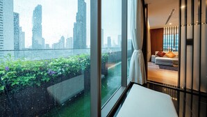 Habitación de hotel moderna con un ventanal grande que da a un paisaje urbano y un jardín.