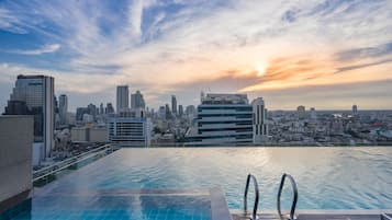 Piscina infinita com vista para o horizonte urbano ao pôr do sol.