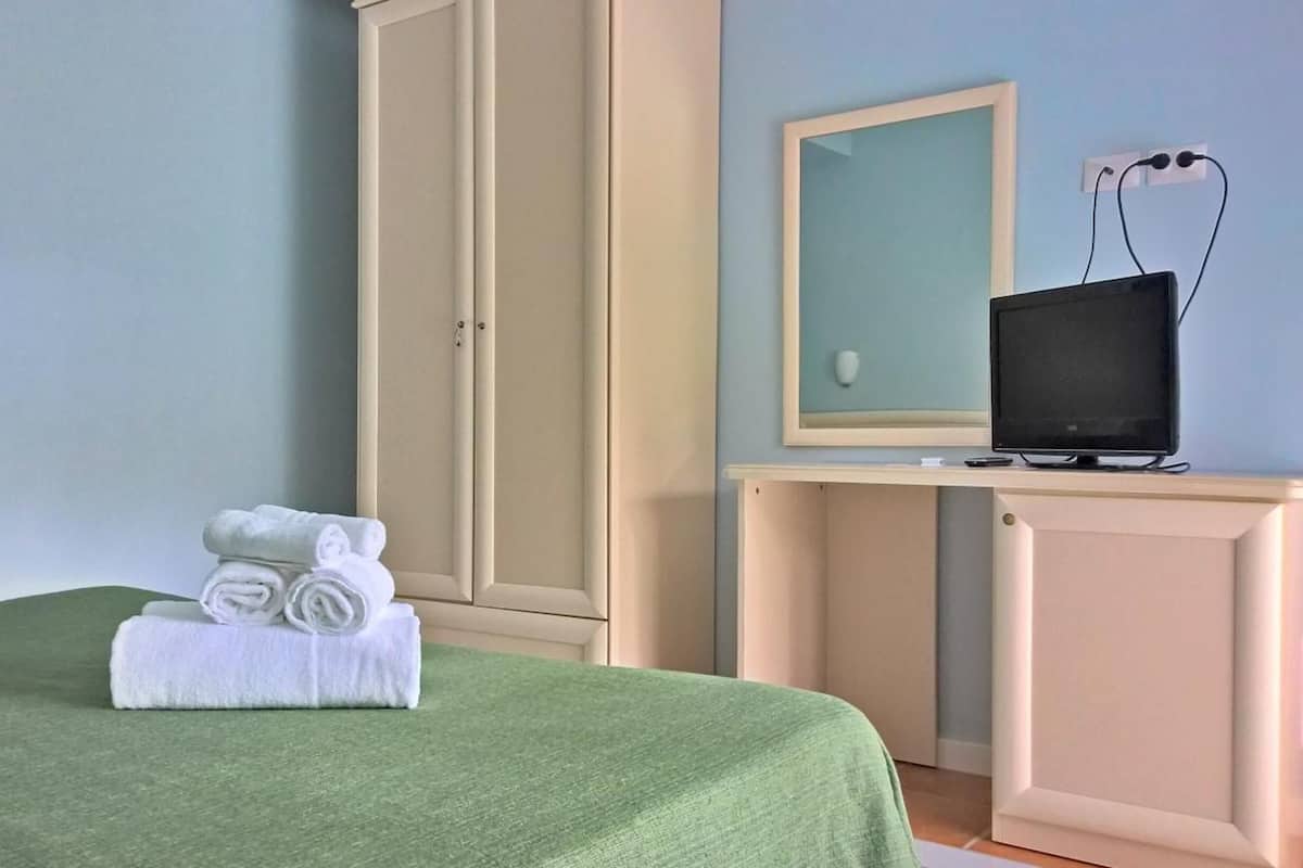 Un letto rifatto con una coperta verde e una pila di asciugamani bianchi sopra.