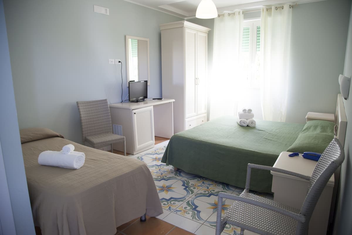 Camera d'albergo con due letti, una scrivania con un computer, una sedia e un armadio.