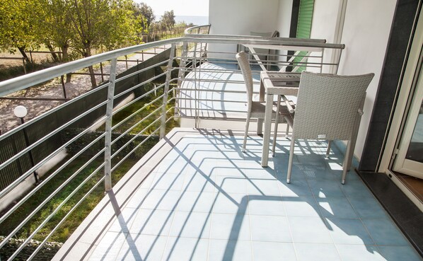 Un balcón con barandilla de metal, una silla de mimbre y vista al mar.