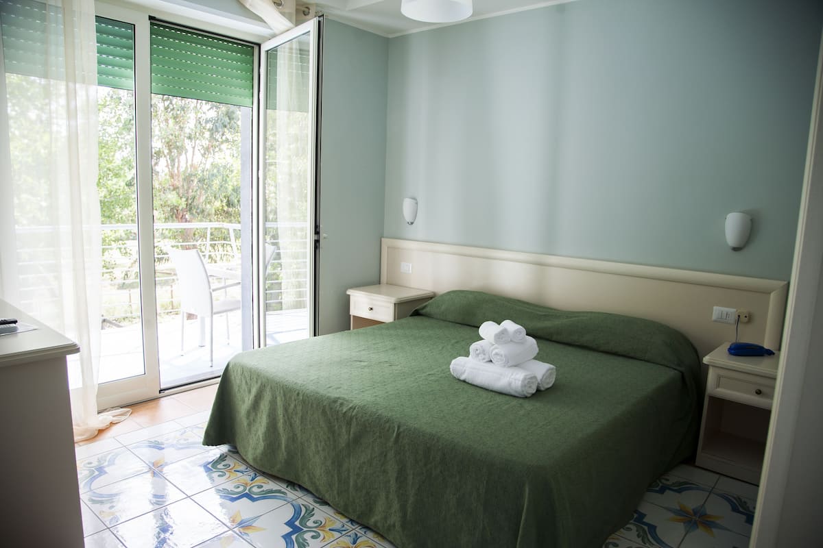 Una camera da letto con una coperta verde, un comodino e una vista attraverso una porta scorrevole in vetro.