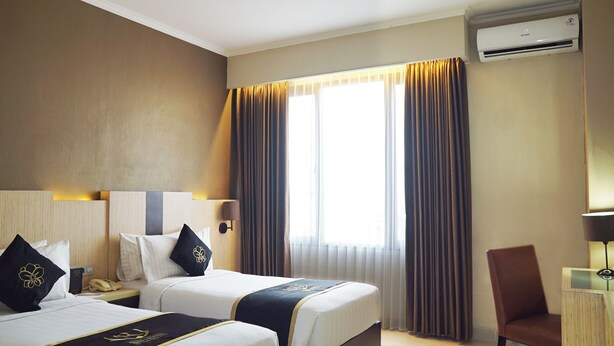 A hotel room with two beds, a desk, a chair, an air conditioning unit, and a window with curtains. - Riss Hotel Malioboro (Yogyakarta)