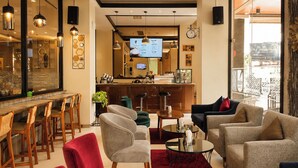 A modern hotel lobby with a bar area, seating arrangements, and a television screen displaying a menu. - Riss Hotel Malioboro (Yogyakarta)