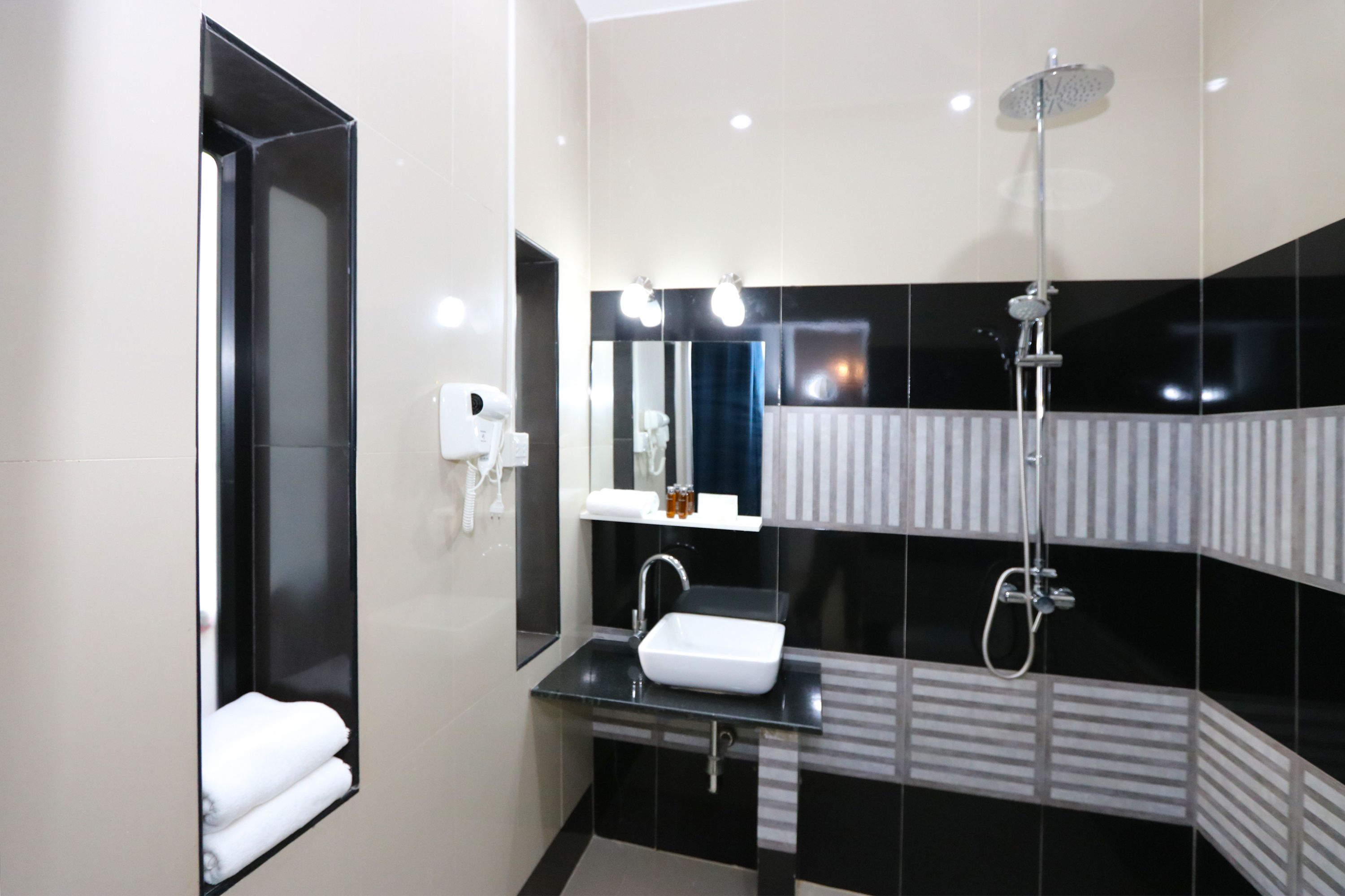 Un baño moderno con pared de azulejos blanco y negro, un lavamanos blanco, un espejo y una ducha.
