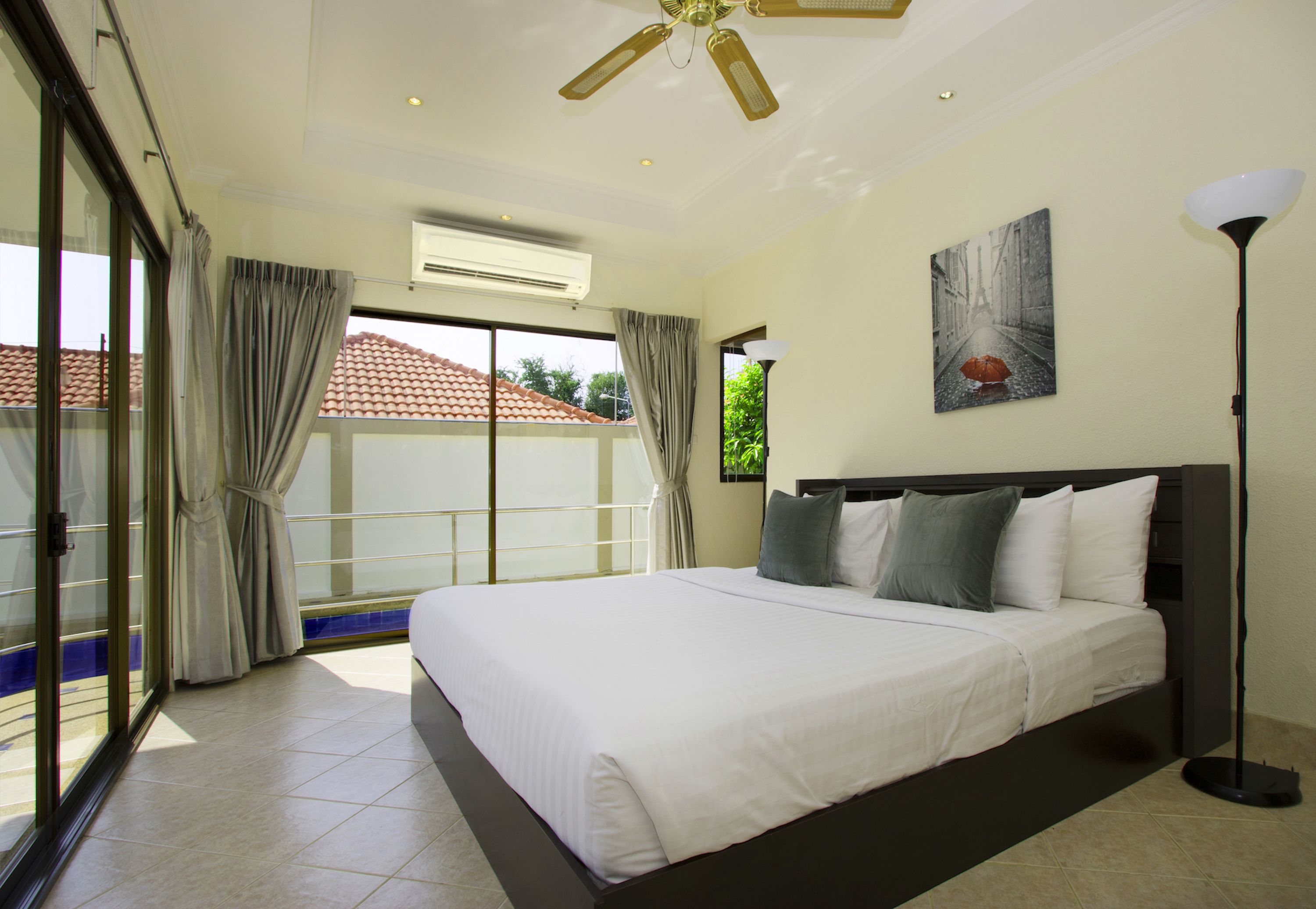 A spacious bedroom with a large bed, a ceiling fan, an air conditioning unit, and a view through a sliding glass door to the outside.