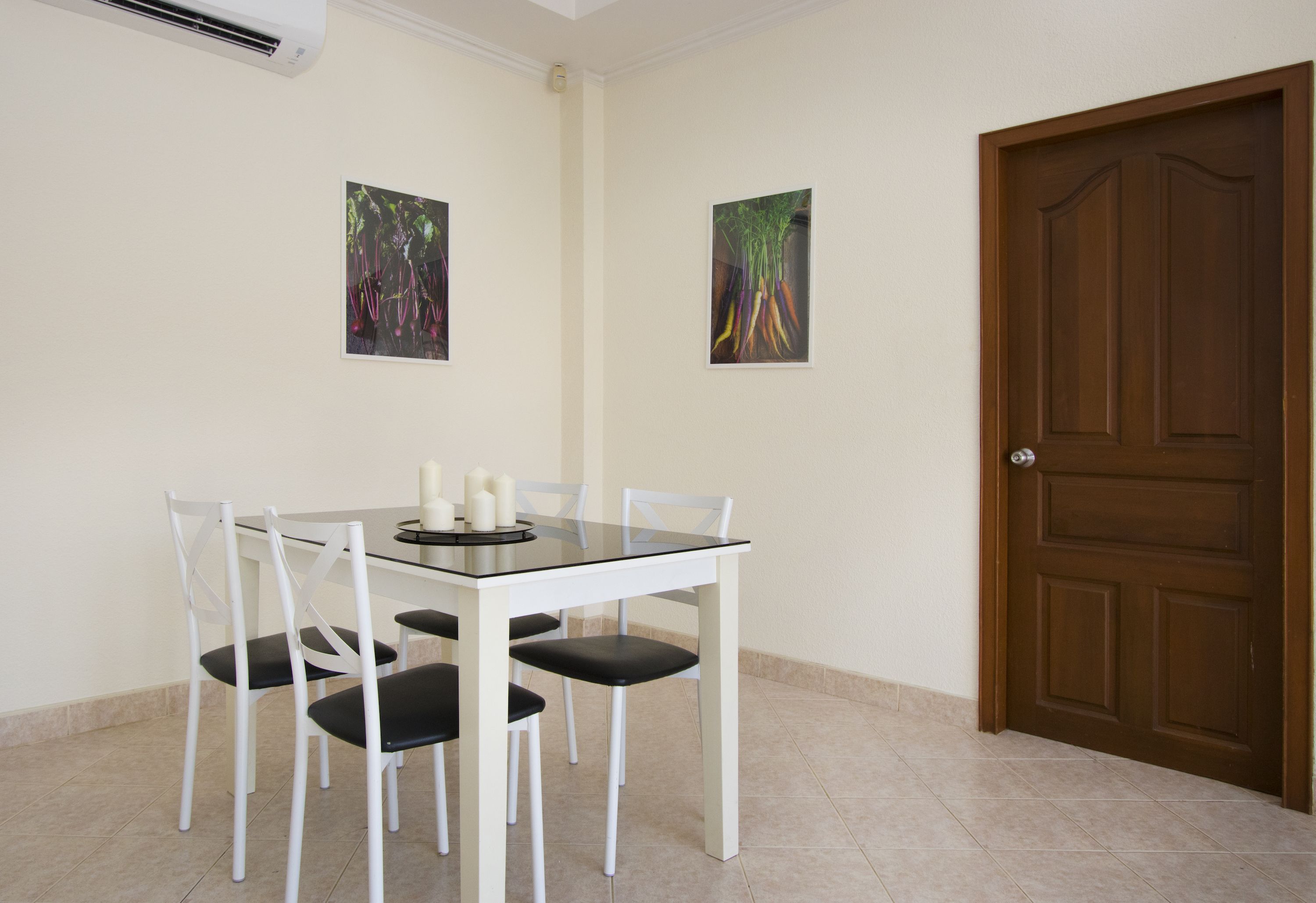A dining area with a glass table, white chairs, and two paintings on the wall.