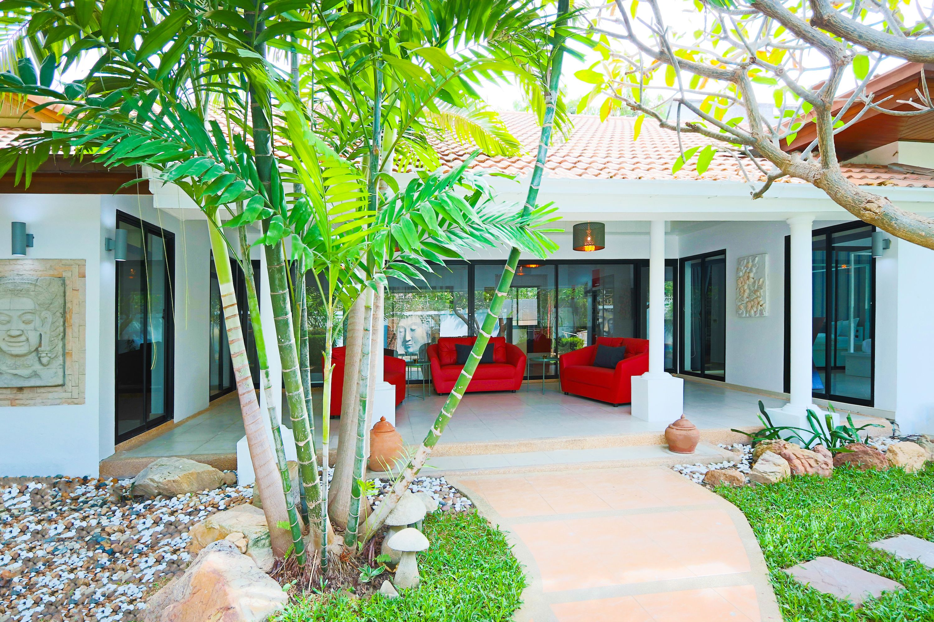 Una casa moderna con un espacio exterior cubierto, muebles rojos y un jardín con rocas y plantas.