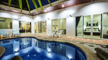 A swimming pool with lounge chairs and a table, surrounded by glass doors and a patio area.