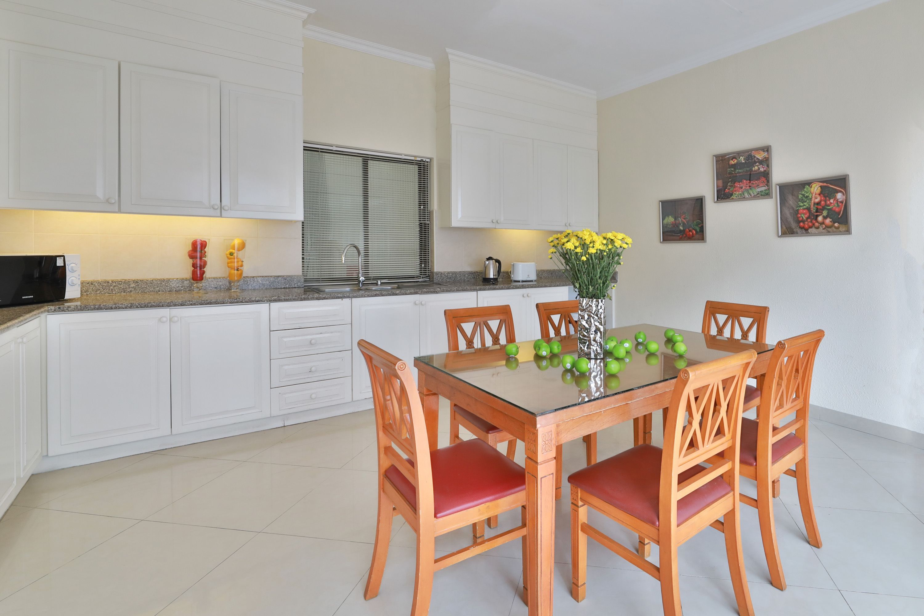 A modern kitchen with white cabinets, a glass-top dining table, and wooden chairs.