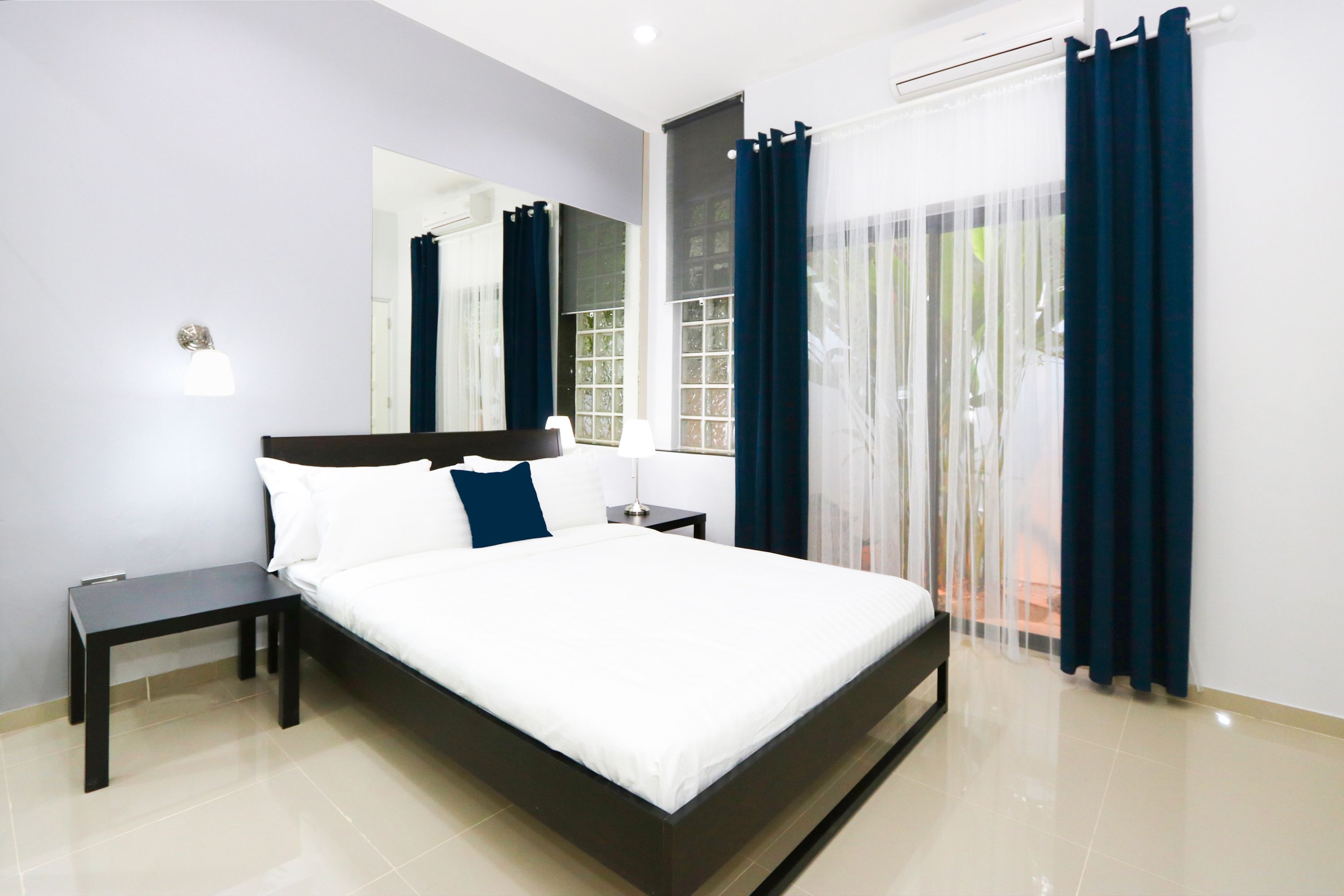 Une chambre d’hôtel moderne avec un grand lit, une table de chevet, une commode, un miroir et une fenêtre avec des rideaux.