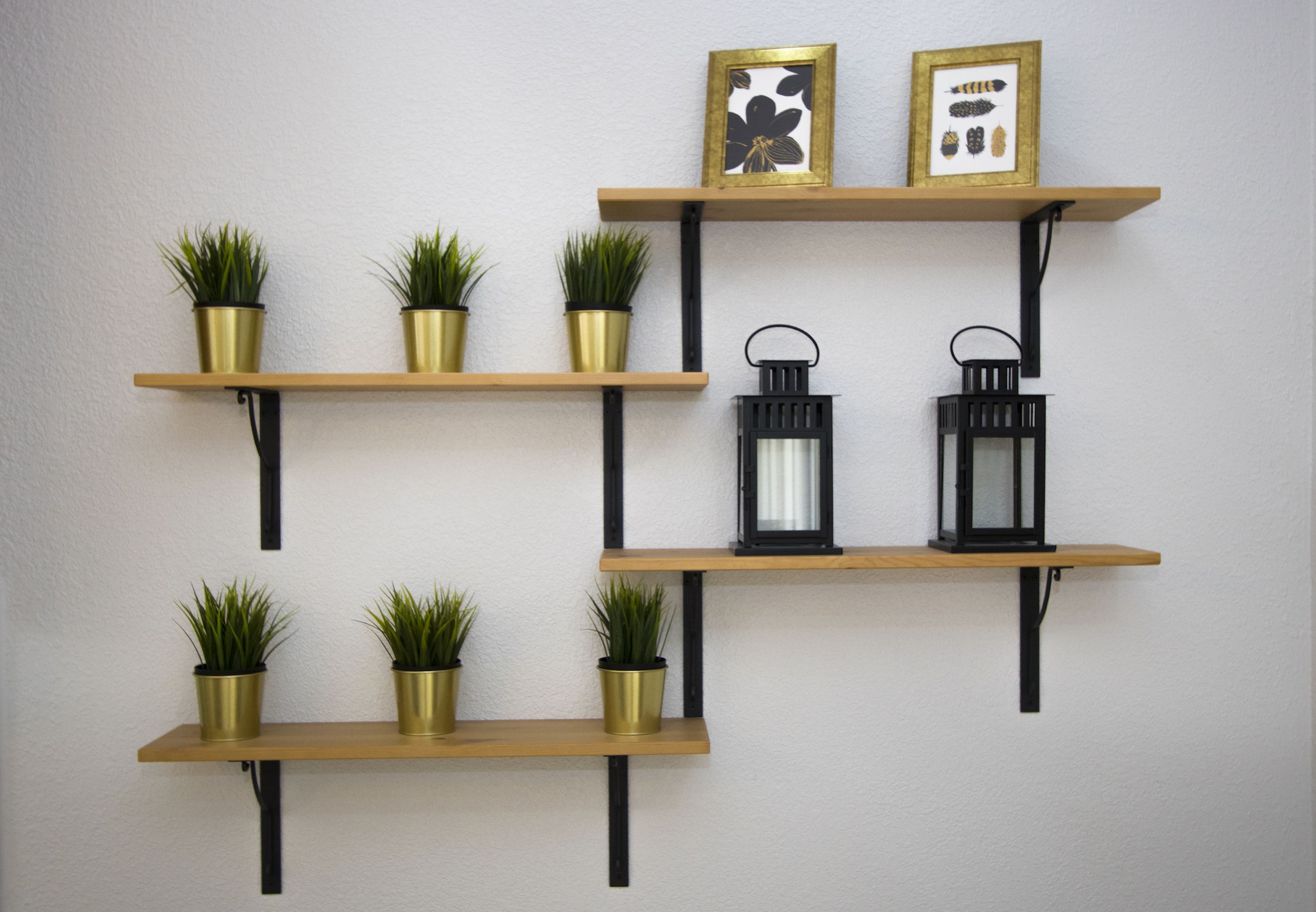 A wall-mounted shelf unit with three shelves, each holding potted plants and decorative items.