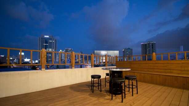 A rooftop bar with a wooden deck, bar stools, and a round table. - Empathy Guesthouse - Hostel (Daegu)