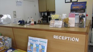 A reception area with a wooden counter, a sign labeled "RECEPTION," and various informational brochures and pamphlets. - Empathy Guesthouse - Hostel (Daegu)