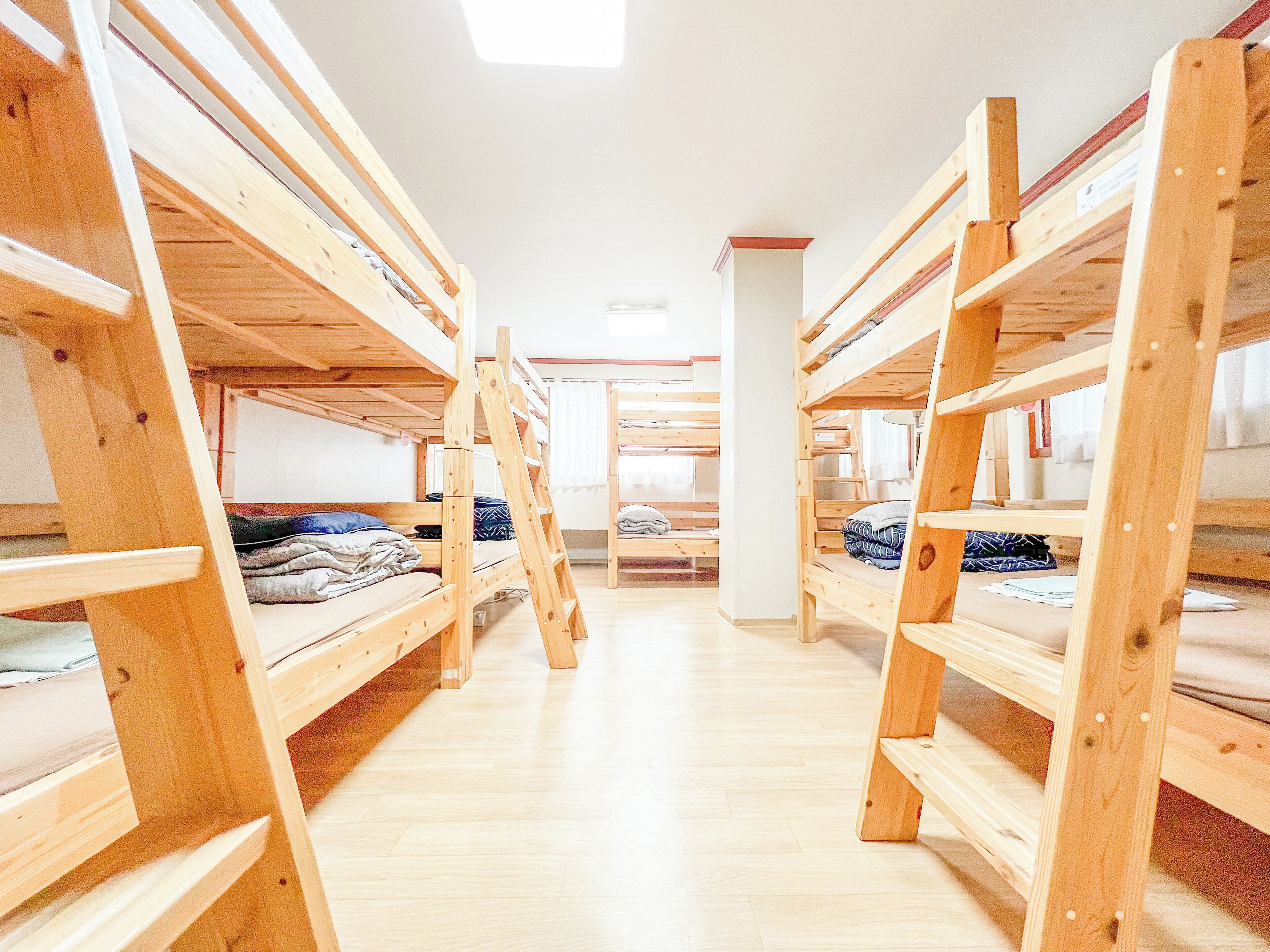 A dormitory with bunk beds arranged in rows, wooden floors, and a central pillar.