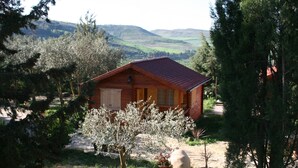 Una cabaña de madera con techo rojo, rodeada de árboles y vistas a colinas ondulantes.