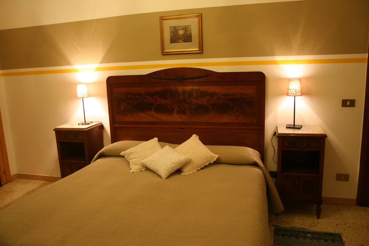 A neatly made bed with a wooden headboard, two bedside tables with lamps, and a framed picture on the wall.