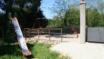 Kids can play on the slide, swings, and explore the playground surrounded by trees.