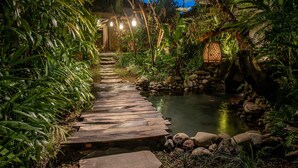 A wooden pathway leading to a pond surrounded by lush greenery and rocks. - Aryaswara Villa Ubud (Ubud)