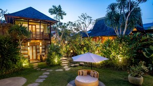 A tropical resort with a well-maintained garden, a circular seating area with an umbrella, and a building with a balcony. - Aryaswara Villa Ubud (Ubud)