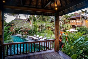 Terraza de madera con piscina, sillas de descanso y exuberante vegetación tropical.