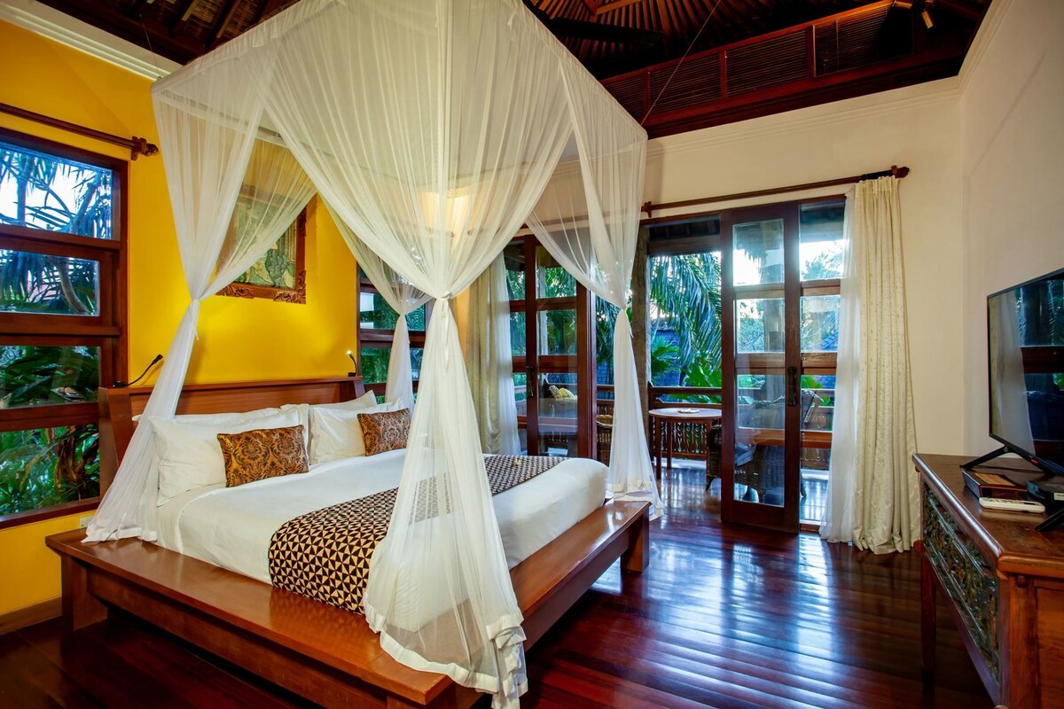 A bedroom with a four-poster bed, a television, and a view of the outdoors.