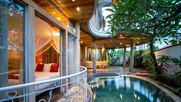 A luxurious bedroom with a large bed, a balcony with a white railing, and a view of a swimming pool. - Aryaswara Villa Ubud (Ubud)