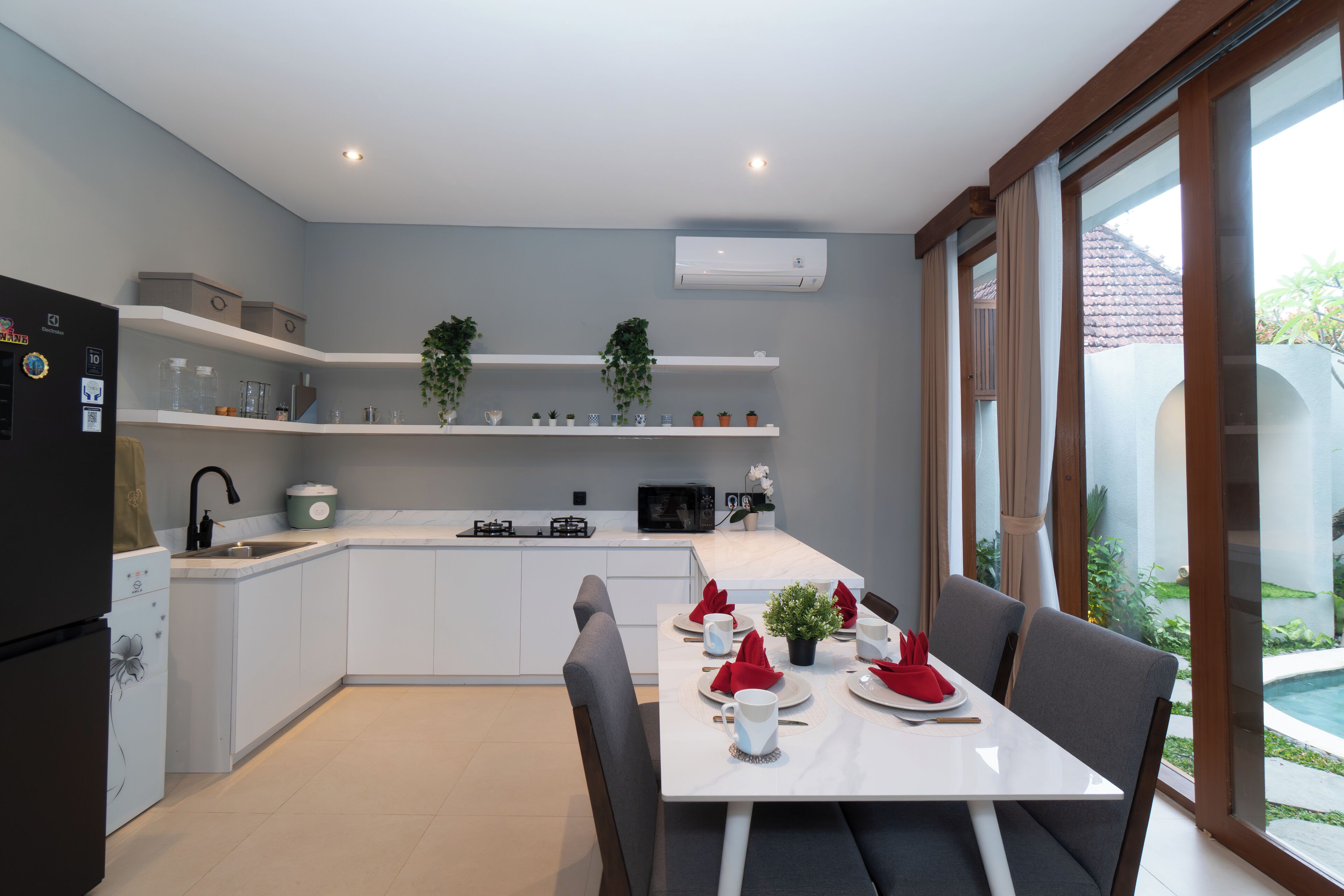 A modern kitchen with white cabinets, a dining table set for four, and a view of a swimming pool.