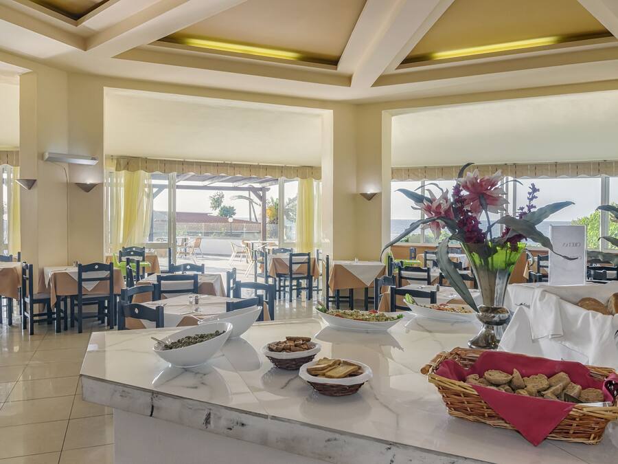 Un comedor con mesas dispuestas para el desayuno, con cuencos de cereales, bollería y un jarrón decorativo con flores.