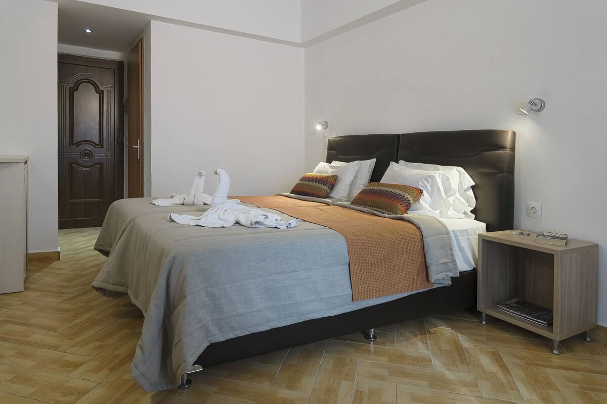 A modern hotel room with a large bed, a bedside table, and a wooden door.