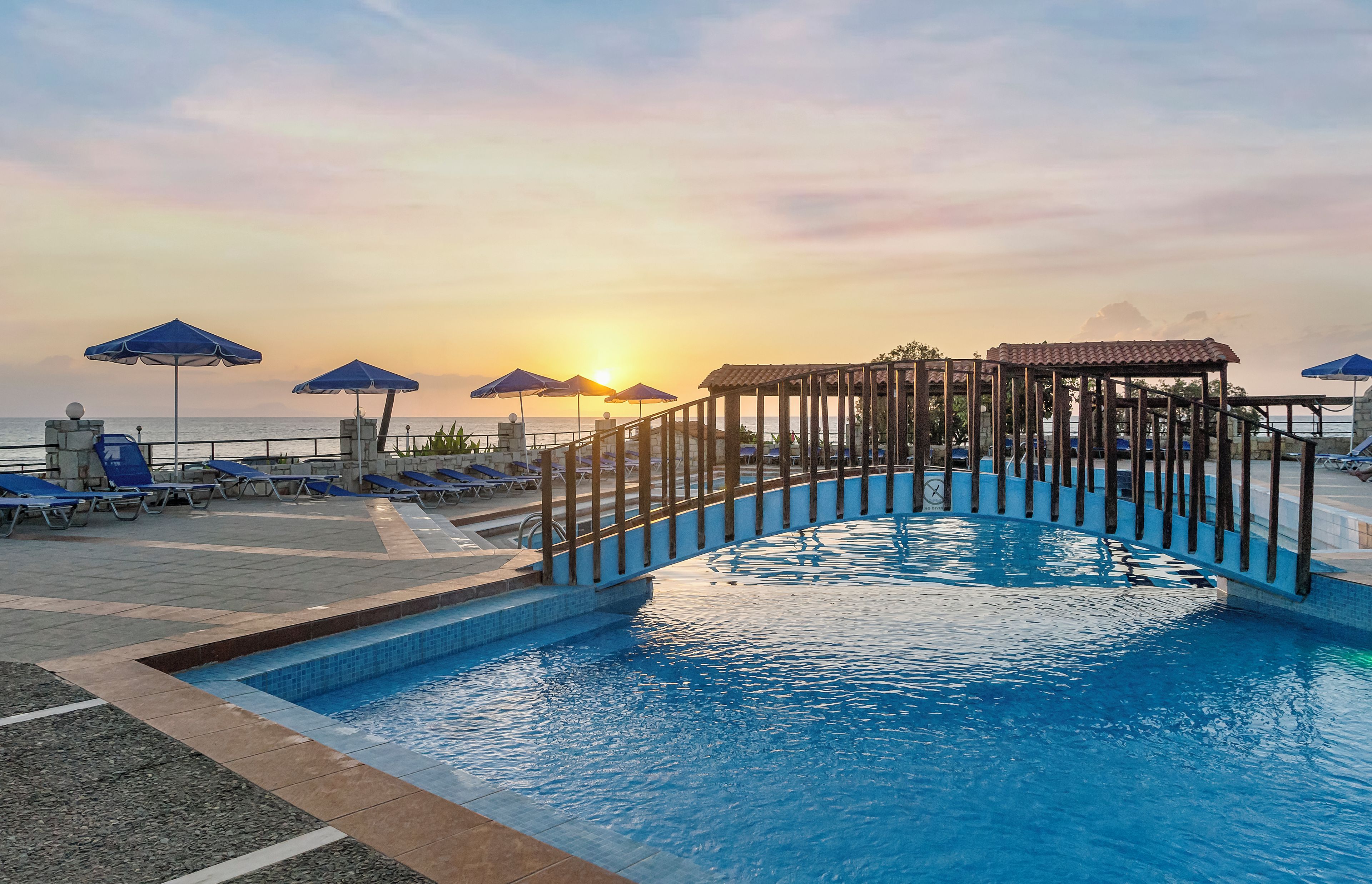 A swimming pool with a wooden structure in the center, surrounded by lounge chairs and umbrellas.