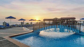 A swimming pool with a wooden structure in the center, surrounded by lounge chairs and umbrellas.