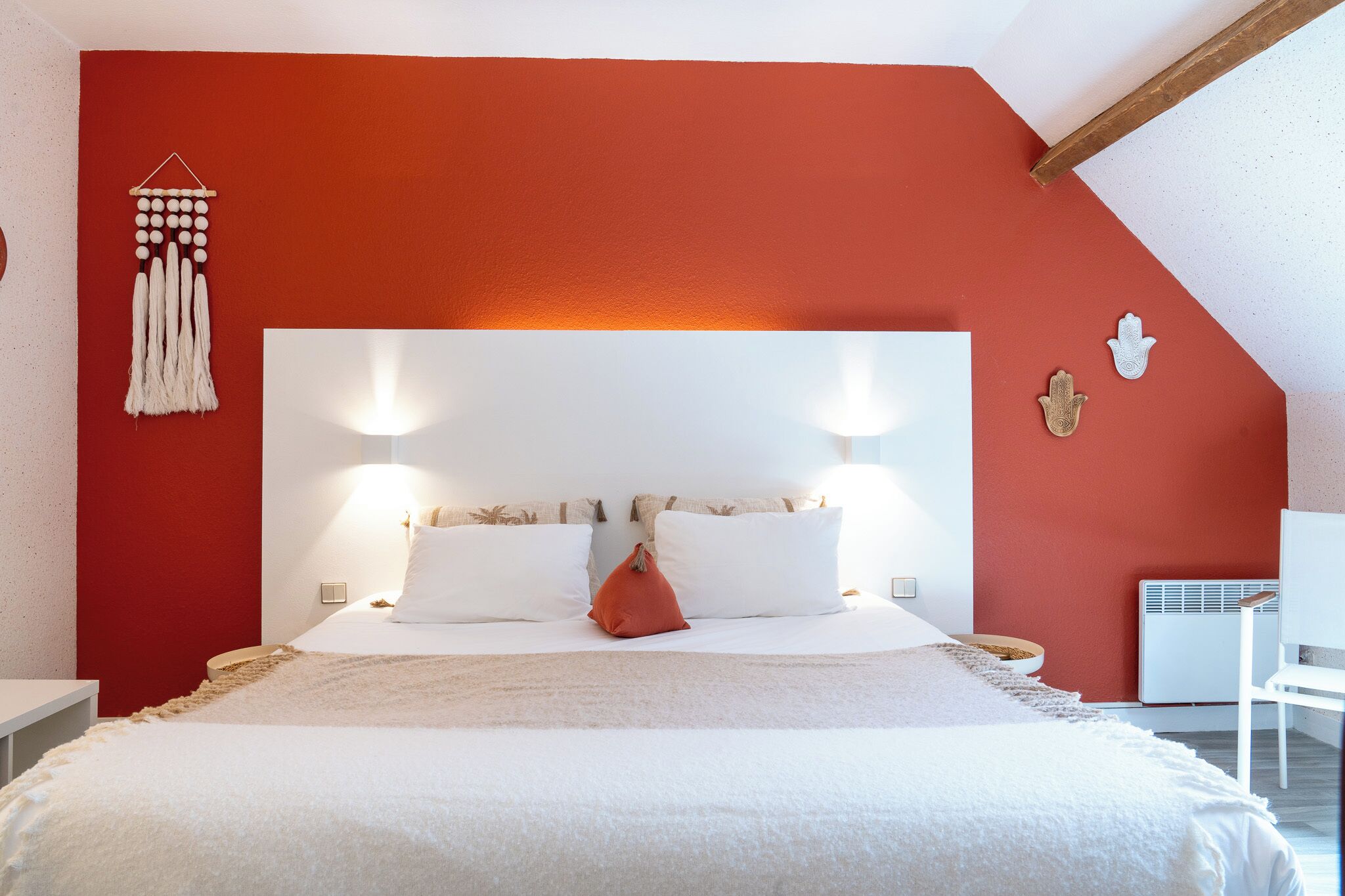 A bedroom with a red accent wall, a white headboard, two bedside lamps, and a bed with white bedding and a red accent pillow.