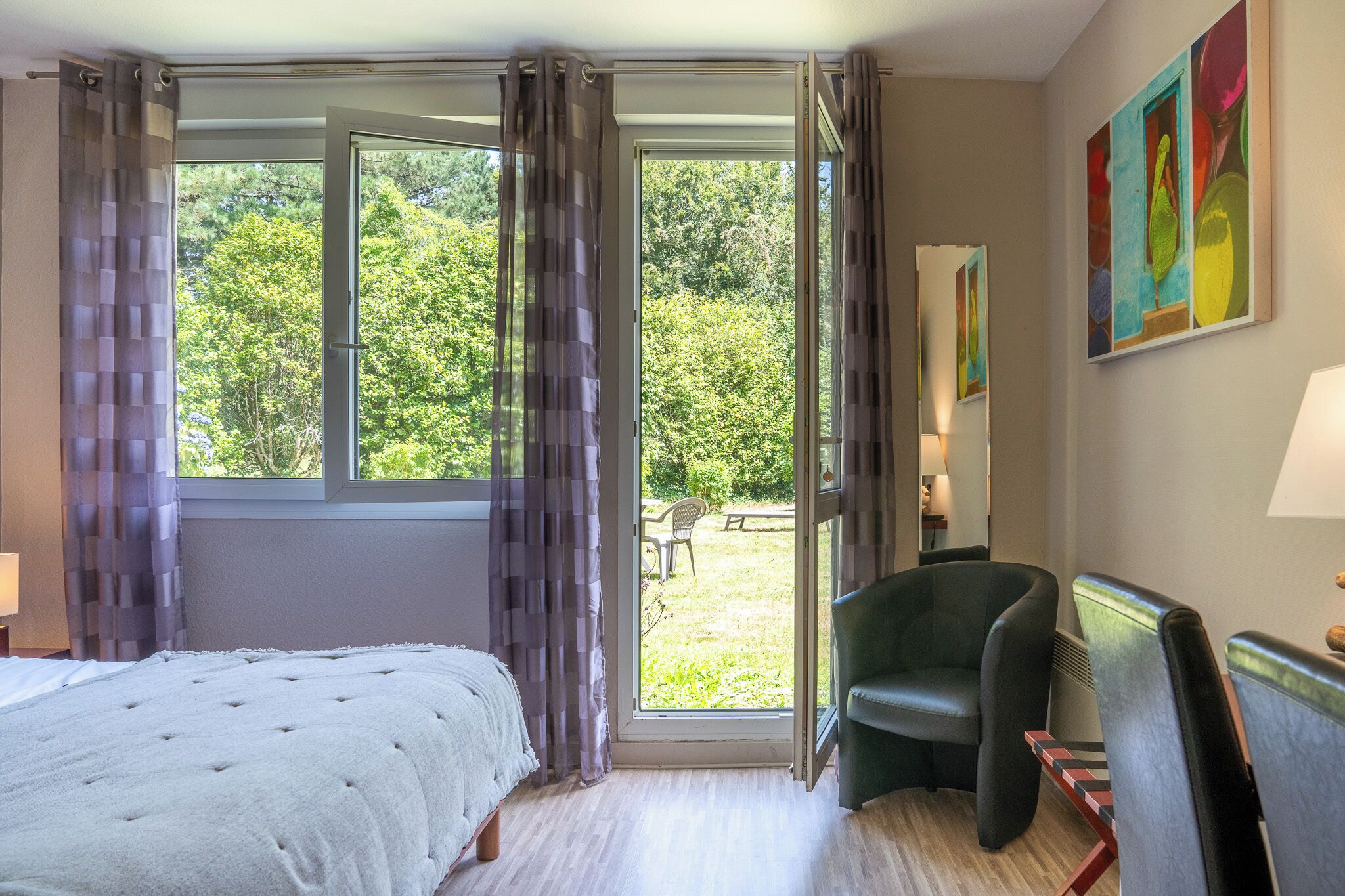 A hotel room with a bed, a chair, a desk, and a view of the outdoors.