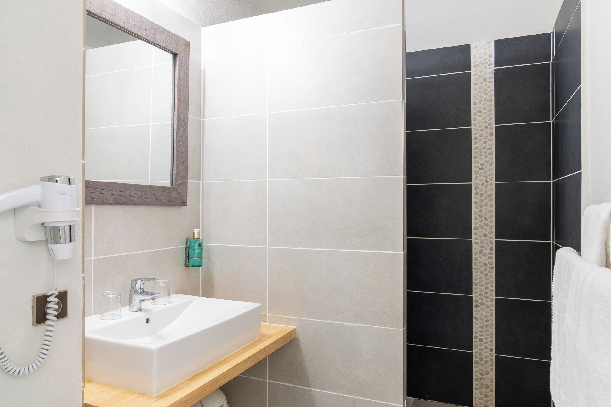 Un baño con lavamanos blanco, un espejo, un secador de pelo y un toallero.
