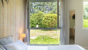 A bedroom with a large window, a bed, a bedside lamp, and a view of a garden.