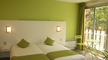 A hotel room with two beds, a small table, a chair, and a balcony with a view of trees.
