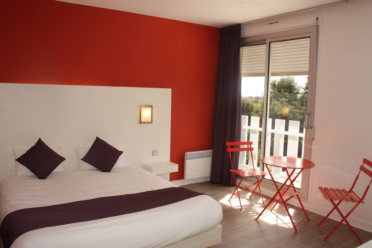 A hotel room with a large bed, a small table, and two chairs.