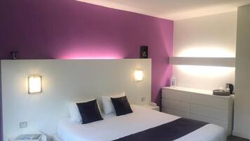 Una habitación de hotel con una cama grande, mesitas de noche y una mesita auxiliar.