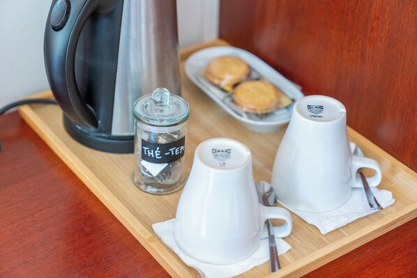 Una preparación de café con una cafetera, un tarro de cristal con la etiqueta 'THÉ-TEA' y dos tazas blancas sobre una bandeja de madera.