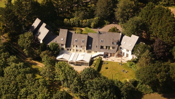 An aerial view of a large, multi-story building surrounded by dense trees and a grassy area. - Hotel Latitude Ouest (Locronan)