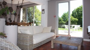 A modern living room with a wicker sofa, a wooden coffee table, and a large sliding glass door leading to an outdoor patio. - Hotel Latitude Ouest (Locronan)