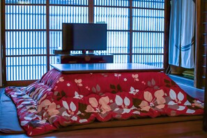 Um quarto japonês tradicional com tatames, uma mesa baixa com televisão e um shoji ao fundo.